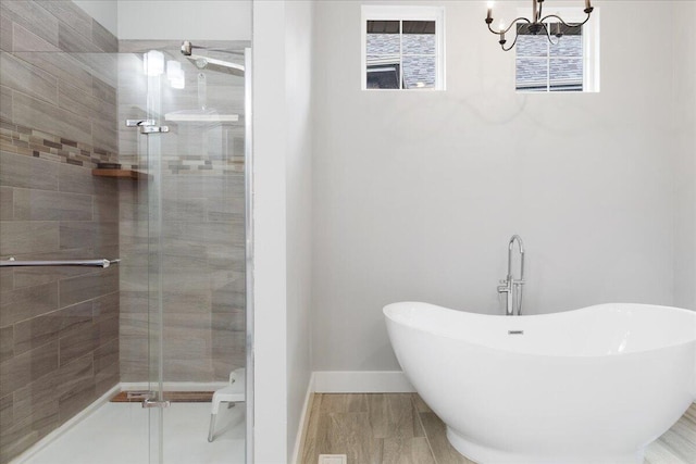 full bathroom featuring a stall shower, a notable chandelier, a freestanding bath, and baseboards