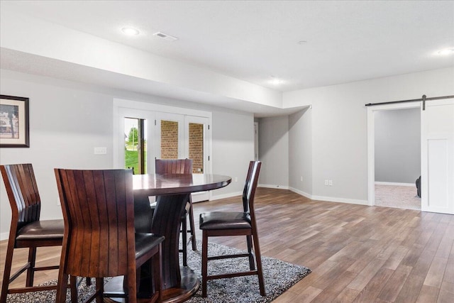 dining space featuring a barn door, baseboards, visible vents, and wood finished floors