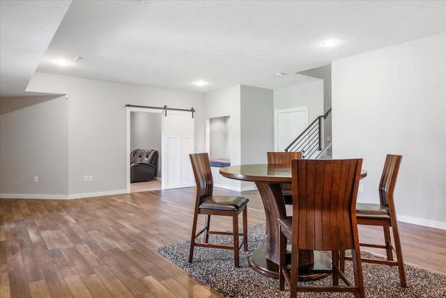 dining area with a barn door, wood finished floors, baseboards, and stairs