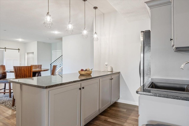 kitchen featuring dark wood finished floors, a peninsula, pendant lighting, and a sink
