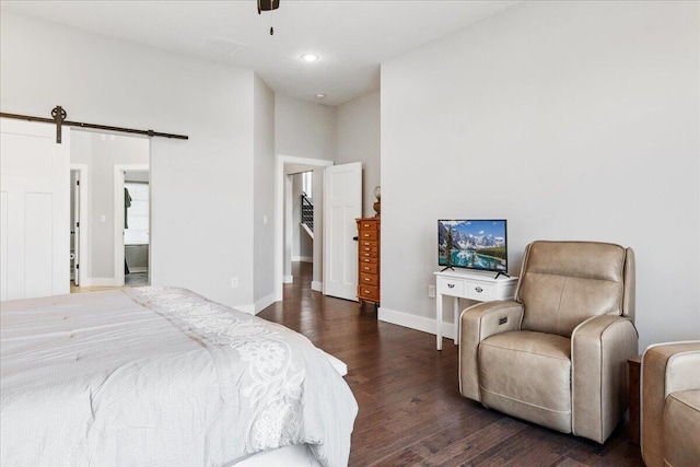 bedroom featuring connected bathroom, wood finished floors, a barn door, baseboards, and ceiling fan