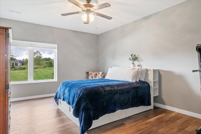 bedroom with a ceiling fan, visible vents, wood finished floors, and baseboards