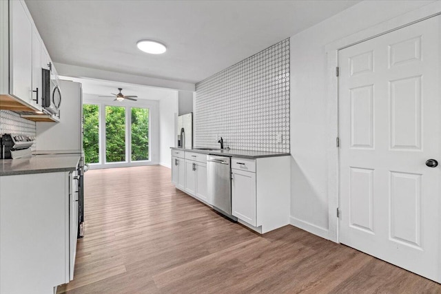 kitchen featuring a ceiling fan, light wood finished floors, a sink, decorative backsplash, and stainless steel appliances