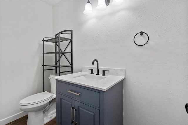 half bath featuring toilet, baseboards, vanity, and wood finished floors