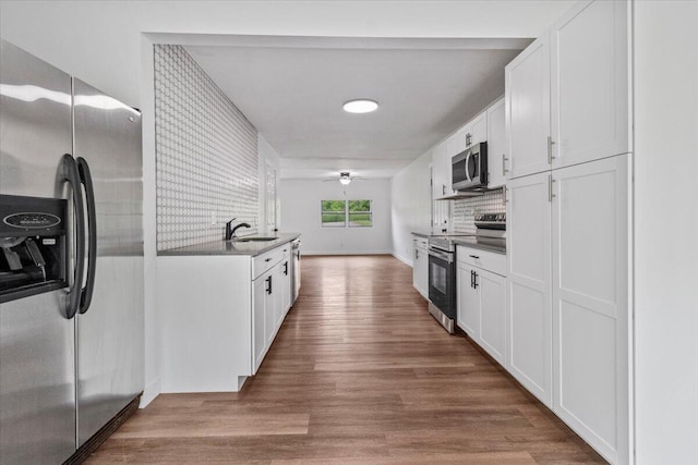 kitchen featuring a sink, stainless steel appliances, wood finished floors, and white cabinets