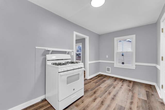 kitchen with white range with gas cooktop, baseboards, visible vents, and wood finished floors