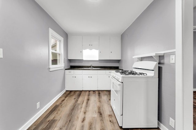 kitchen featuring white range with gas stovetop, a sink, dark countertops, light wood-type flooring, and white cabinetry