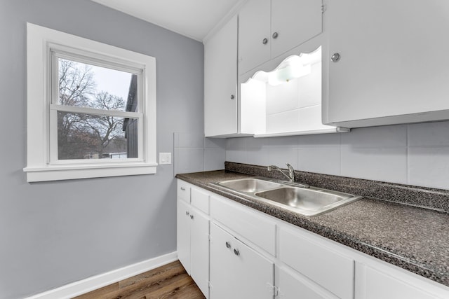 kitchen with dark wood-style flooring, a sink, backsplash, dark countertops, and white cabinets