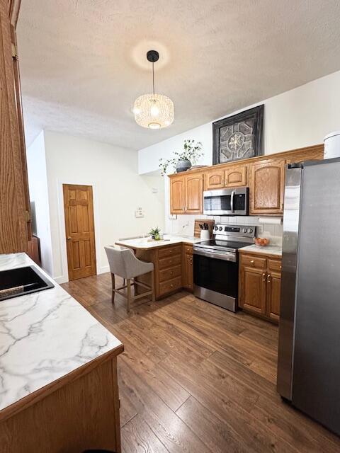 1118 E Ritter St, Republic, MO 65738 - kitchen with decorative light fixtures, dark wood-style flooring, a peninsula, brown cabinets, and stainless steel appliances