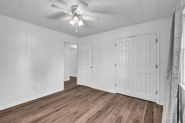 unfurnished bedroom featuring a closet, wood finished floors, baseboards, and ceiling fan