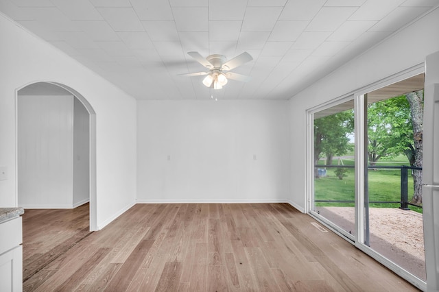 spare room with light wood finished floors, baseboards, a ceiling fan, and arched walkways
