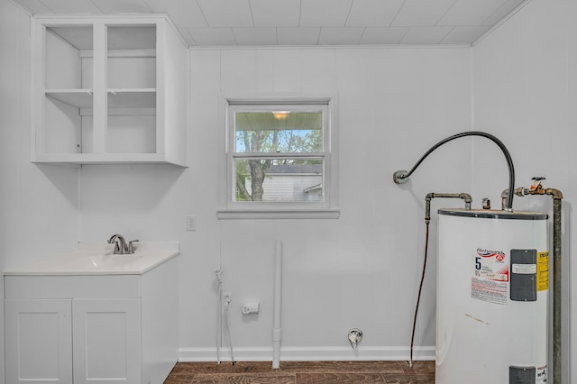 clothes washing area with a sink, water heater, baseboards, and wood finished floors