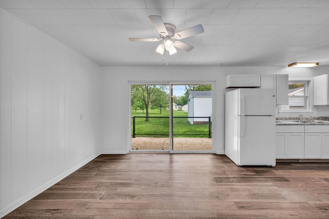 kitchen featuring wood finished floors, a ceiling fan, a sink, freestanding refrigerator, and white cabinets