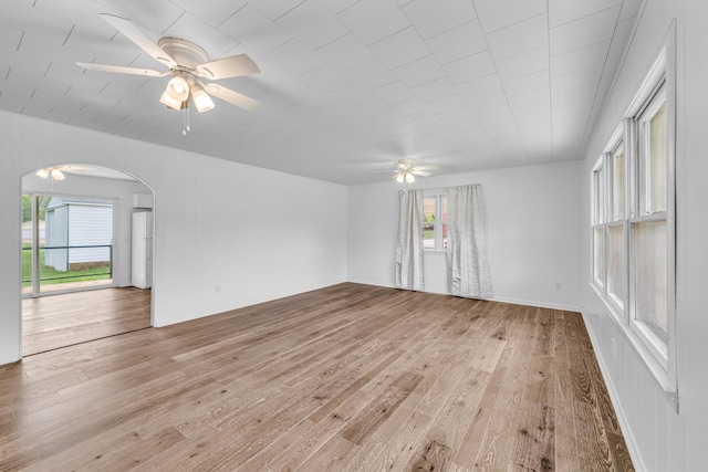 spare room featuring light wood-type flooring, a ceiling fan, and arched walkways