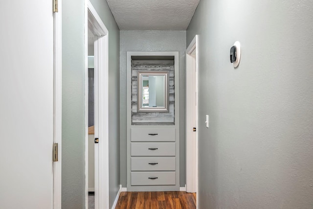 hall with dark wood-style flooring, a textured ceiling, and baseboards
