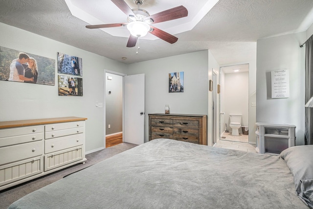 carpeted bedroom with a textured ceiling, ensuite bathroom, baseboards, and a ceiling fan