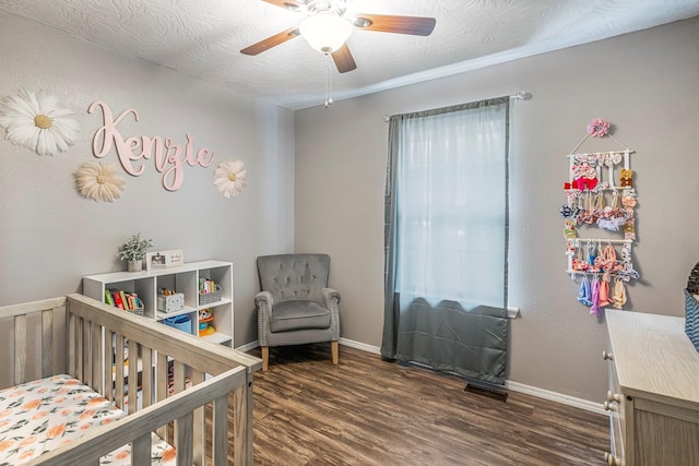 bedroom with ceiling fan, baseboards, a crib, and wood finished floors