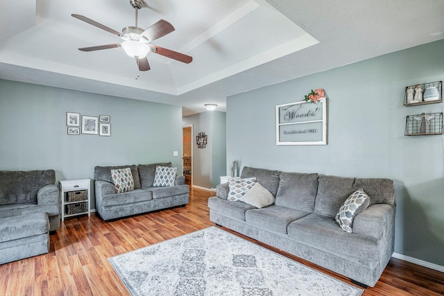 living room featuring a tray ceiling, baseboards, a ceiling fan, and wood finished floors