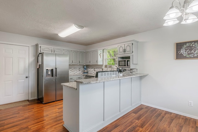 kitchen featuring a peninsula, stainless steel appliances, dark wood-style floors, and a chandelier