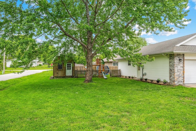 view of yard featuring a storage shed, an attached garage, fence, an outdoor structure, and a playground