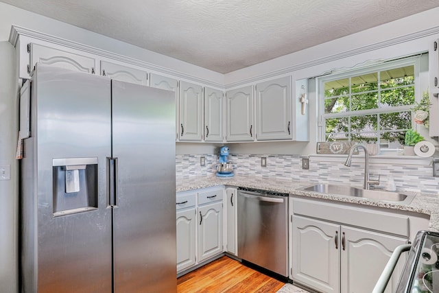 kitchen featuring a sink, tasteful backsplash, appliances with stainless steel finishes, light stone counters, and light wood-style floors