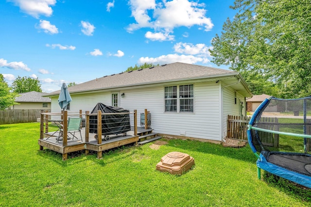 rear view of property featuring a trampoline, a yard, a deck, and a fenced backyard