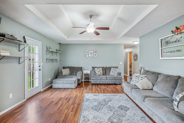 living area with a ceiling fan, baseboards, a tray ceiling, and wood finished floors