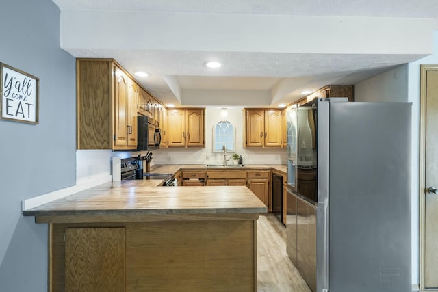 kitchen featuring a sink, a peninsula, black appliances, light countertops, and a raised ceiling