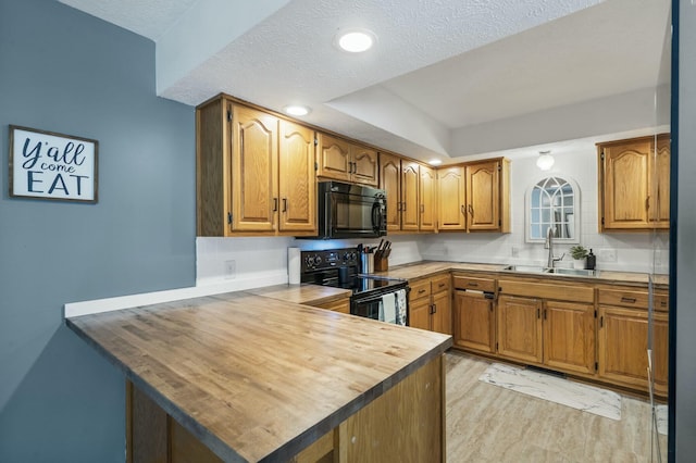 kitchen featuring a peninsula, brown cabinets, a sink, a textured ceiling, and black appliances