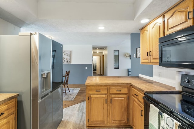 kitchen featuring butcher block countertops, a peninsula, black appliances, recessed lighting, and light wood finished floors