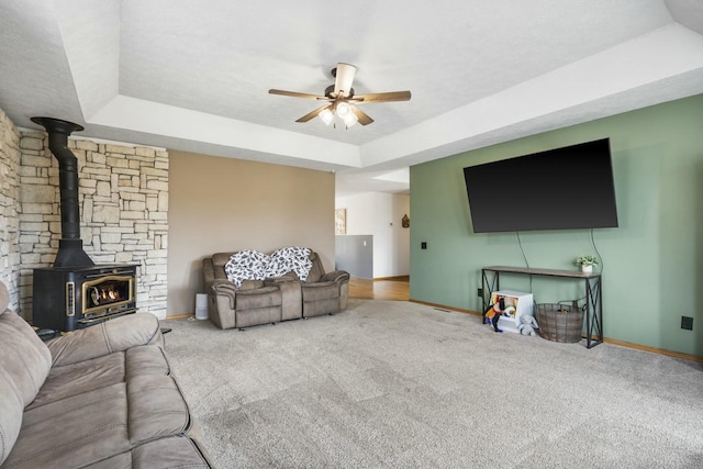 living area with a tray ceiling, baseboards, a ceiling fan, and a wood stove