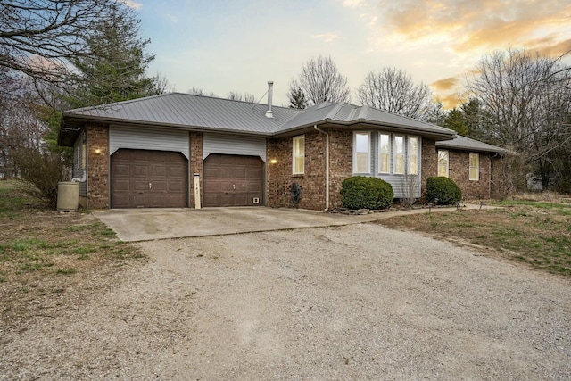 ranch-style home featuring metal roof, a garage, brick siding, and driveway