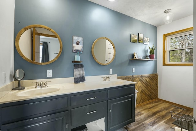 full bathroom with baseboards, double vanity, a sink, and wood finished floors