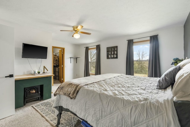 carpeted bedroom featuring multiple windows, a fireplace, a walk in closet, and ceiling fan
