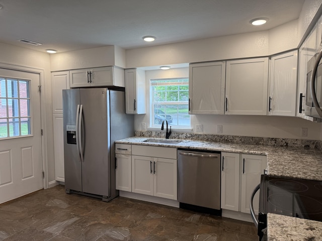 kitchen featuring appliances with stainless steel finishes, visible vents, light stone countertops, and a sink