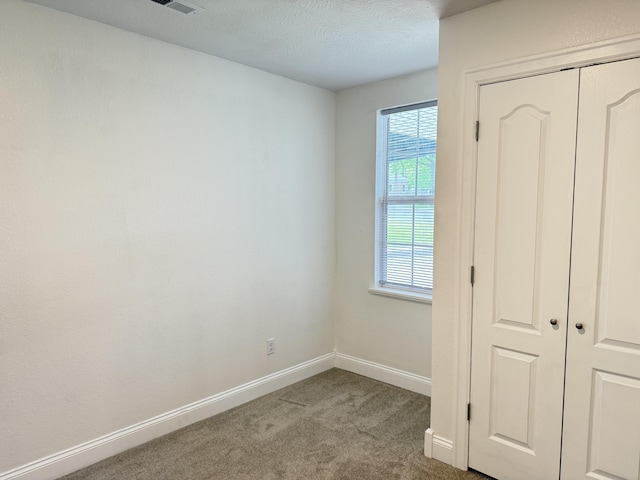 unfurnished bedroom with carpet, a closet, a textured ceiling, visible vents, and baseboards