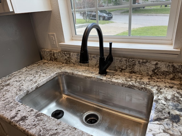 interior details with a sink, a textured wall, and light stone counters