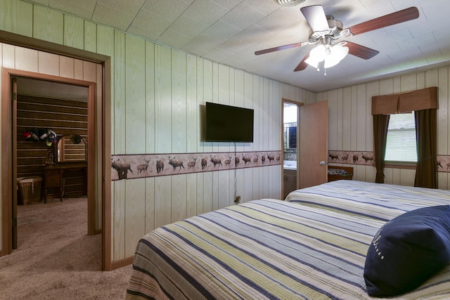 carpeted bedroom with a ceiling fan, wooden walls, and a walk in closet