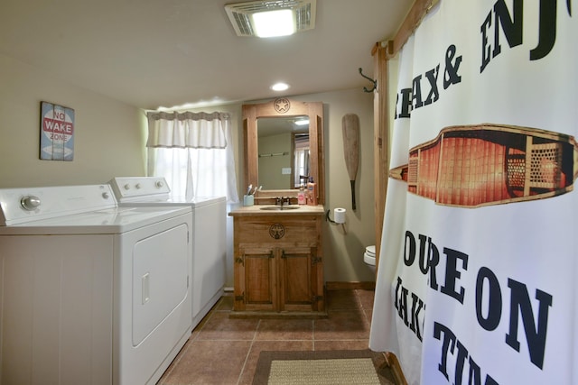 washroom with a sink, laundry area, visible vents, washing machine and clothes dryer, and dark tile patterned flooring