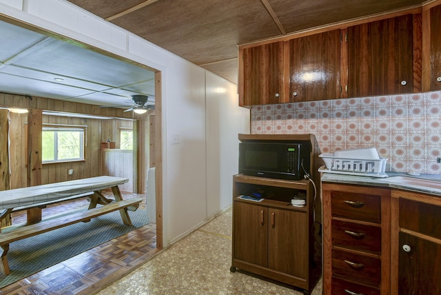 kitchen featuring a ceiling fan, light floors, black microwave, and wooden walls