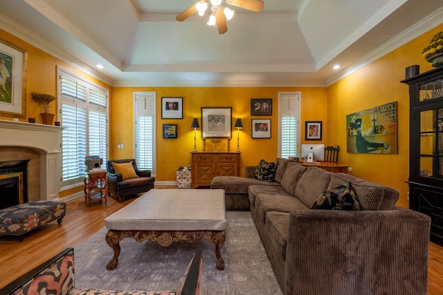 living room featuring a fireplace, ceiling fan, a tray ceiling, and wood finished floors