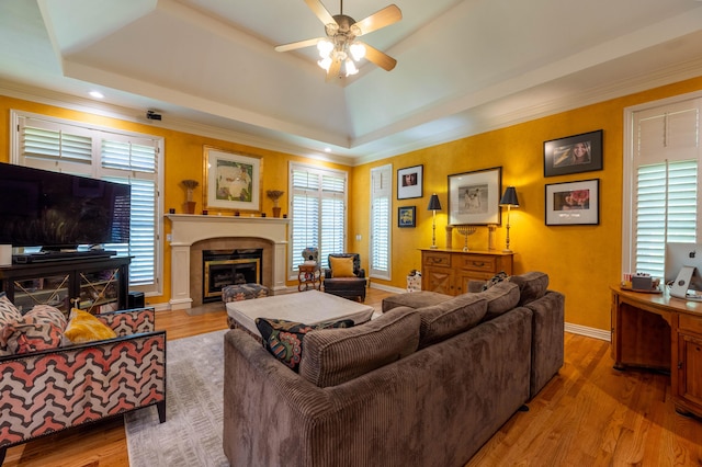 living room featuring a tray ceiling, wood finished floors, a ceiling fan, and a glass covered fireplace