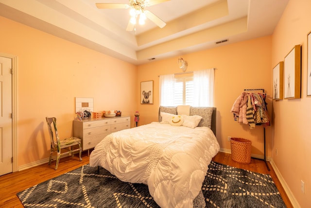 bedroom with a tray ceiling, visible vents, wood finished floors, and baseboards