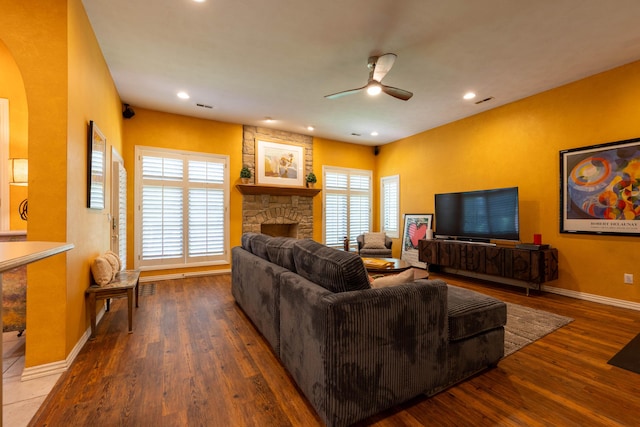 living area with baseboards, a stone fireplace, ceiling fan, wood finished floors, and arched walkways