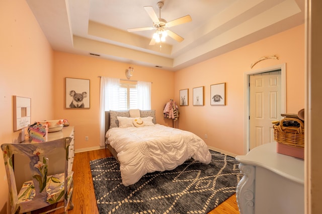 bedroom with wood finished floors, visible vents, a ceiling fan, a raised ceiling, and baseboards
