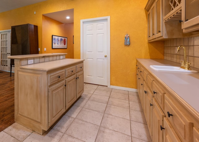 kitchen featuring baseboards, light countertops, a center island, and a sink