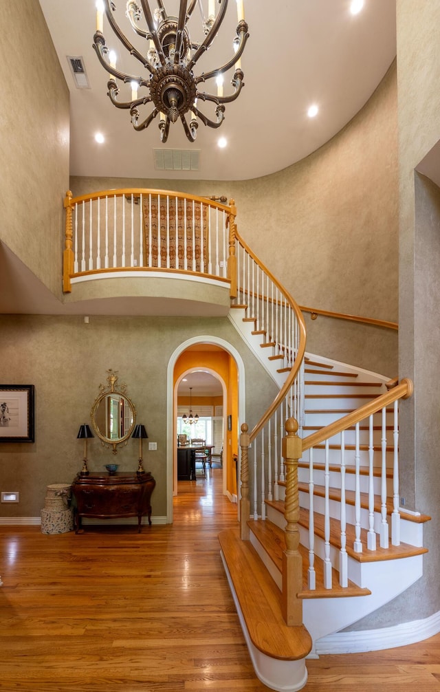 staircase featuring a chandelier, visible vents, wood finished floors, and arched walkways