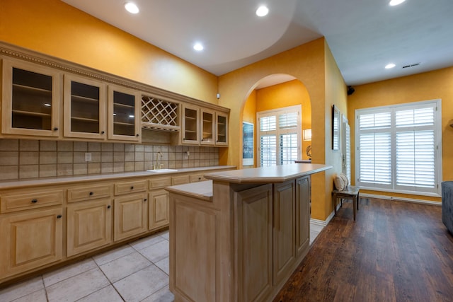 kitchen with a sink, backsplash, light countertops, arched walkways, and a kitchen island
