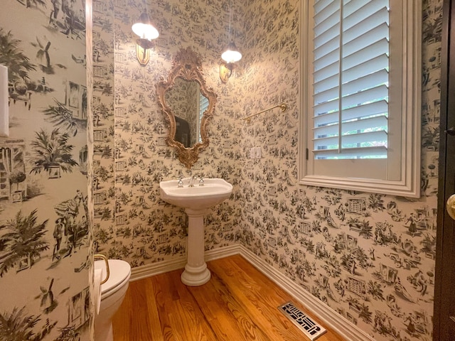 bathroom featuring toilet, wood finished floors, visible vents, baseboards, and wallpapered walls