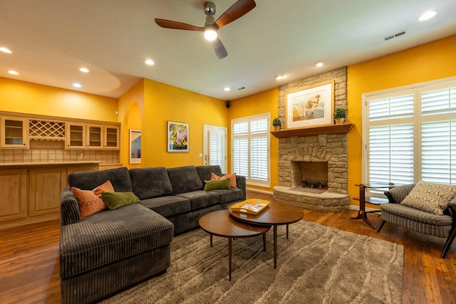 living room with a ceiling fan, a fireplace, visible vents, and wood finished floors